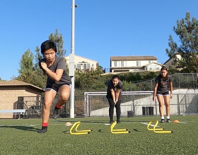 Middle school athletes running agility hurdle drills on an outdoor turf field